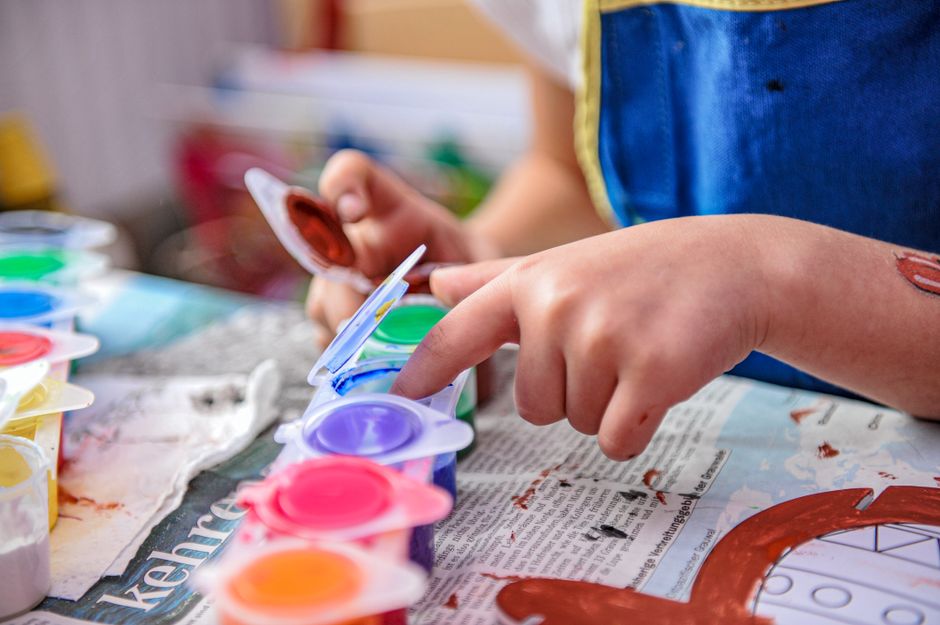 Mãos de criança pintando um desenho com tinta verde e amarela