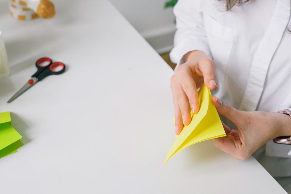 Mãos dobrando uma folha de papel branca sobre a mesa