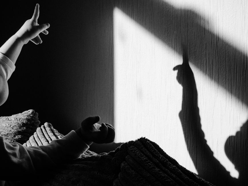 Mão de criança formando a sombra de um bicho na parede com a luz de uma lanterna