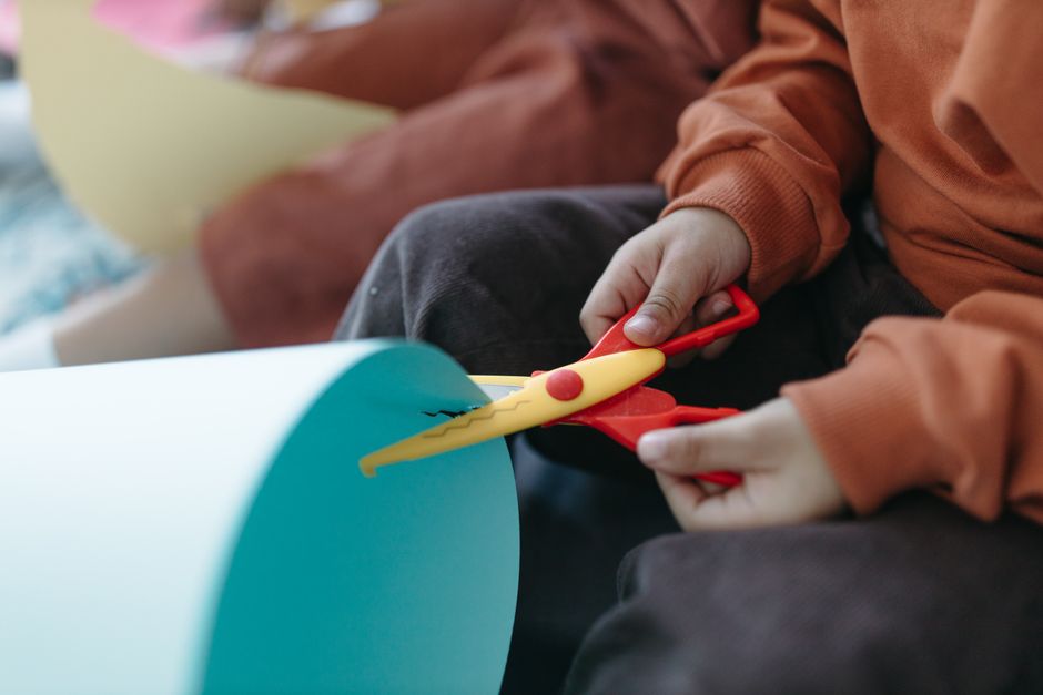 Mãos de criança recortando papel colorido com tesoura sem ponta