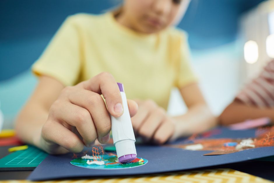 Cola bastão e papéis coloridos organizados numa mesa para atividade infantil