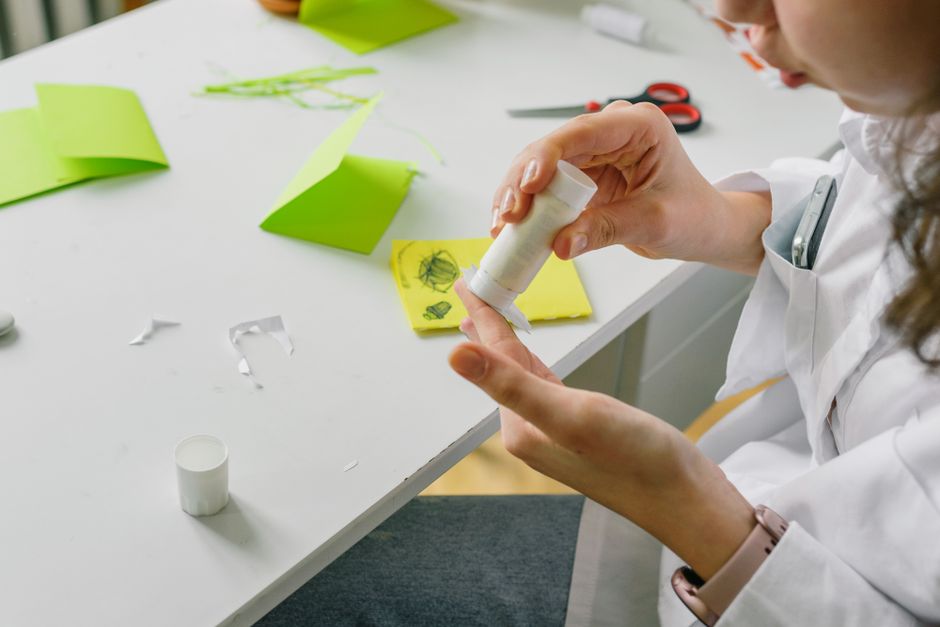 Criança passando cola bastão em papel colorido numa mesa de artesanato