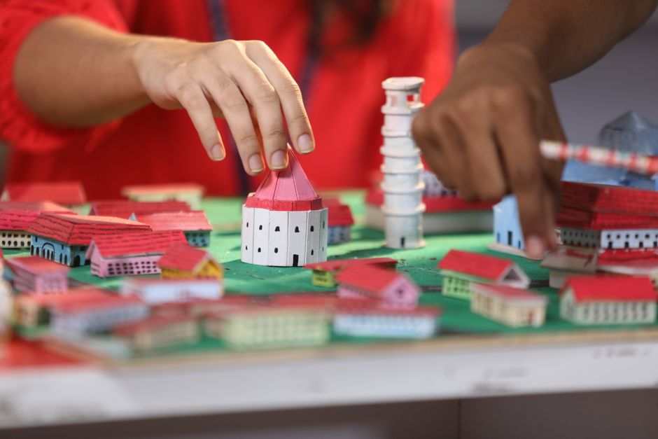 Mãos ajustando peças de um cenário em miniatura montado sobre a mesa
